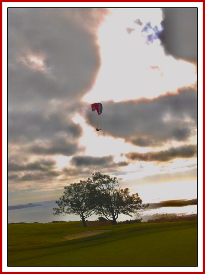 A paraglider above Torrey Pines beneath dramatic clouds